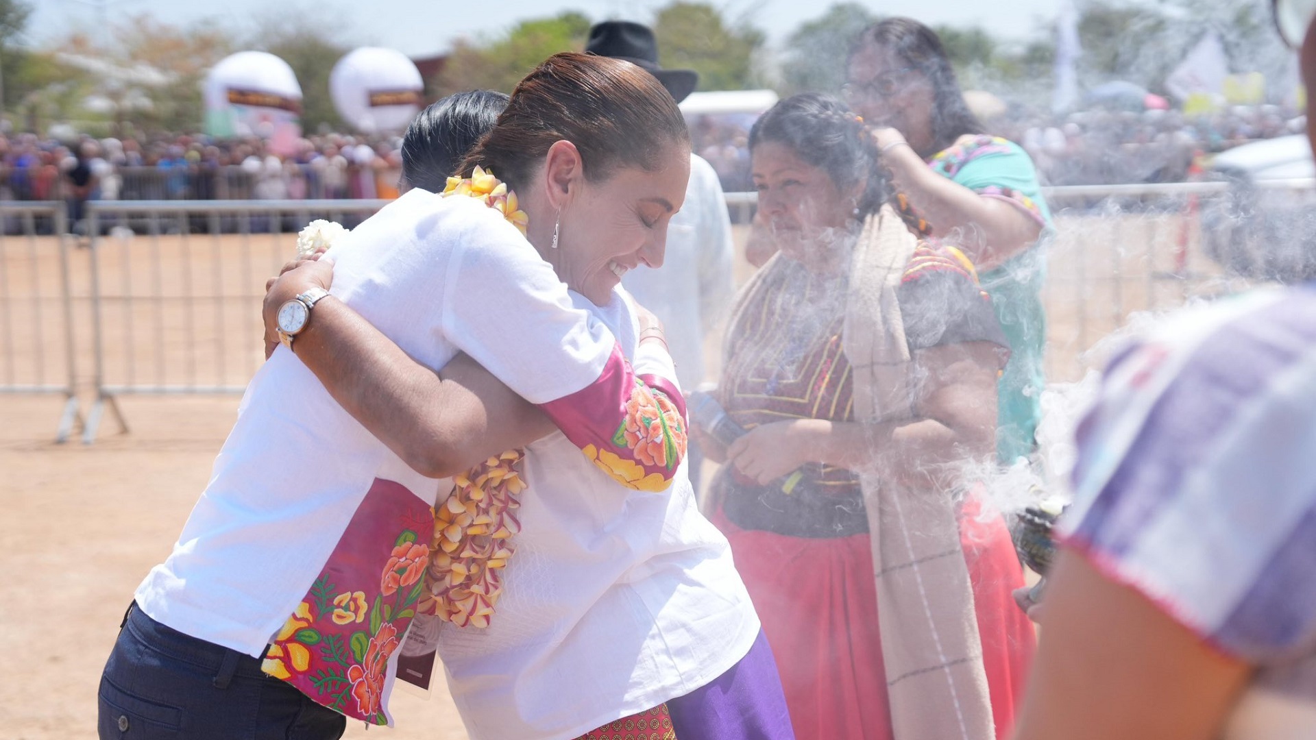 Dos mujeres se abrazan en un ambiente con humo y rodeada de más mujeres.