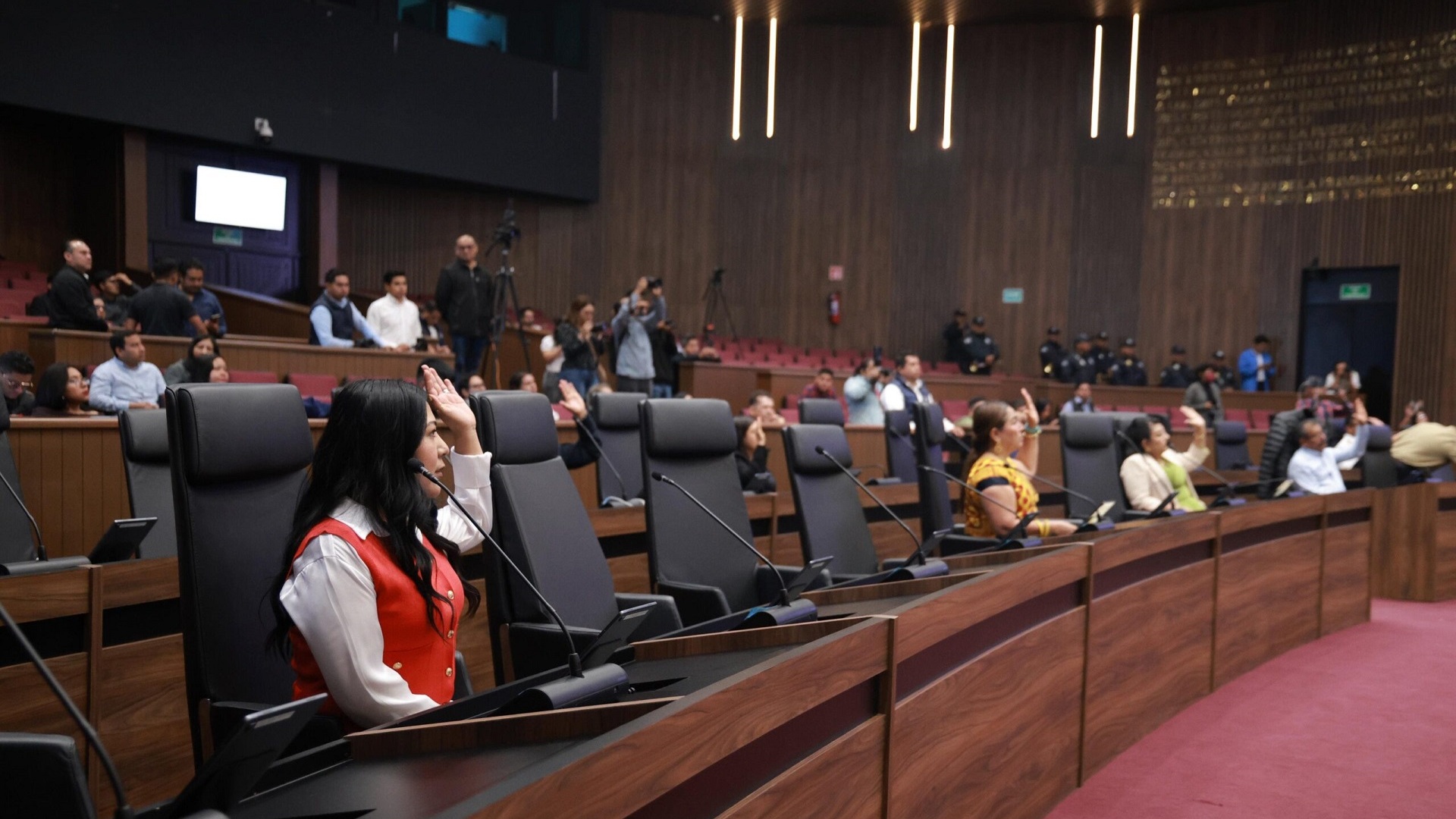 Varias personas sentadas en el Congreso de Oaxaca y levantando la mano en una votación.
