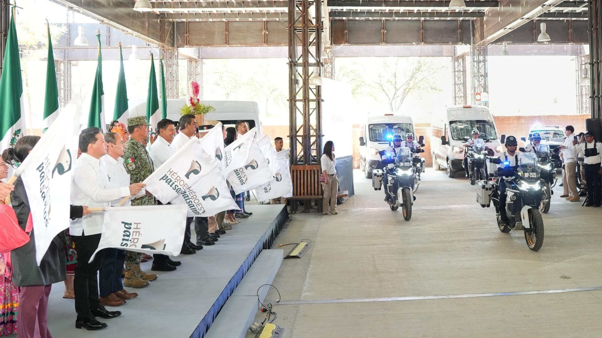 Grupo de personas ondean banderas al paso de policías en motocicletas.