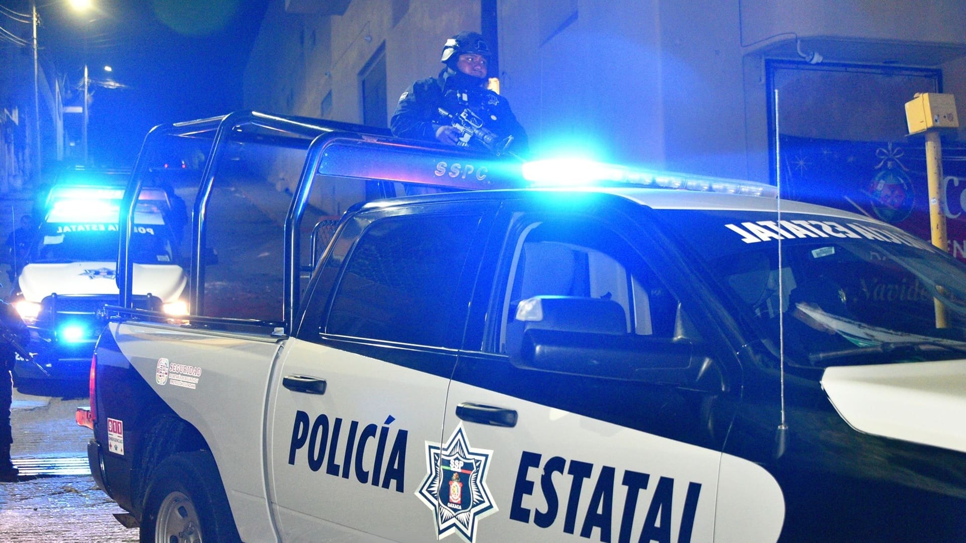 Patrulla de la Policía Estatal de Oaxaca, azul y blanco, con sirenas encendidas.