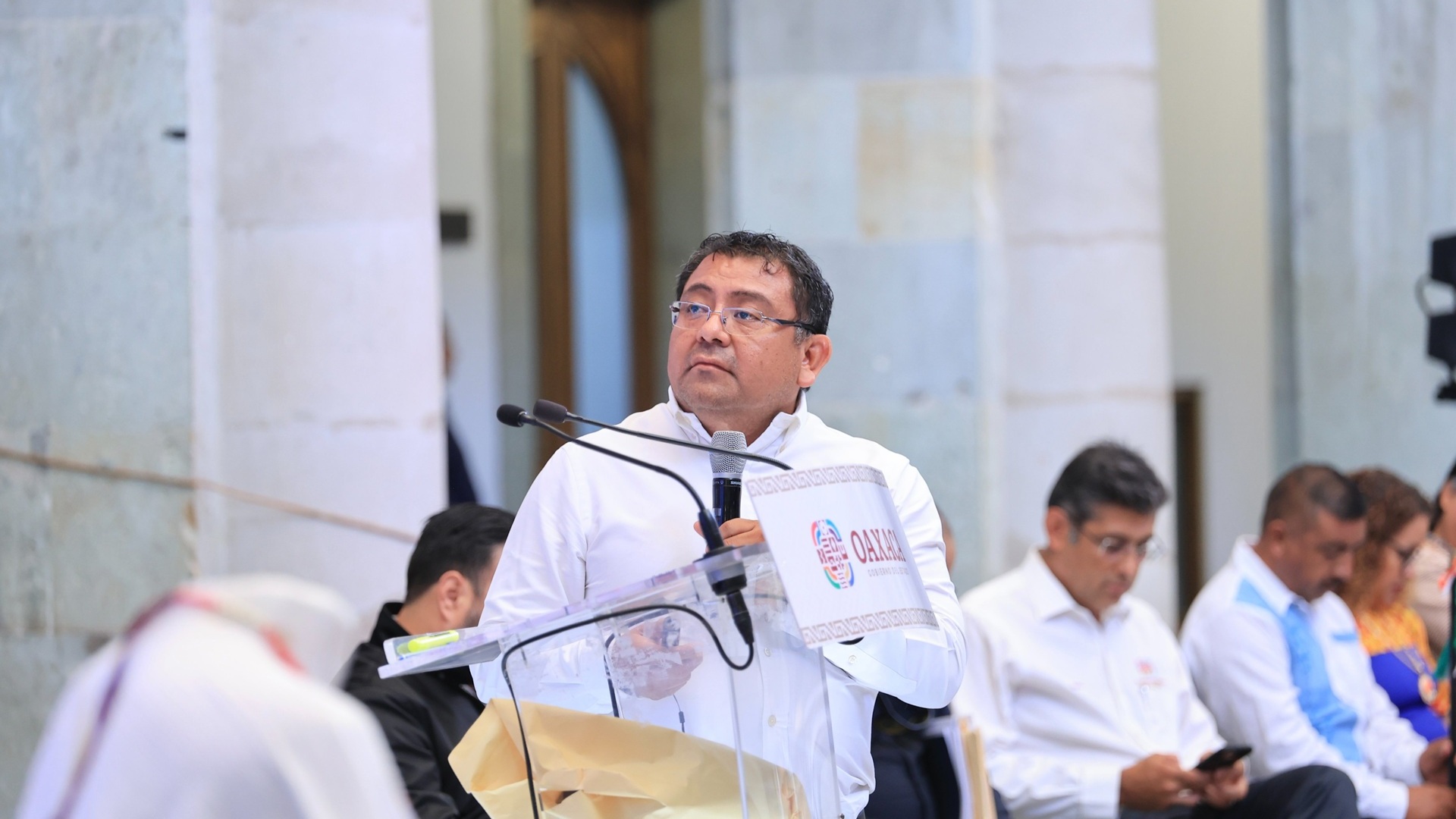 Farid Acevedo hablando con un micrófono en la mano, acompañado de más personas en un auditorio.