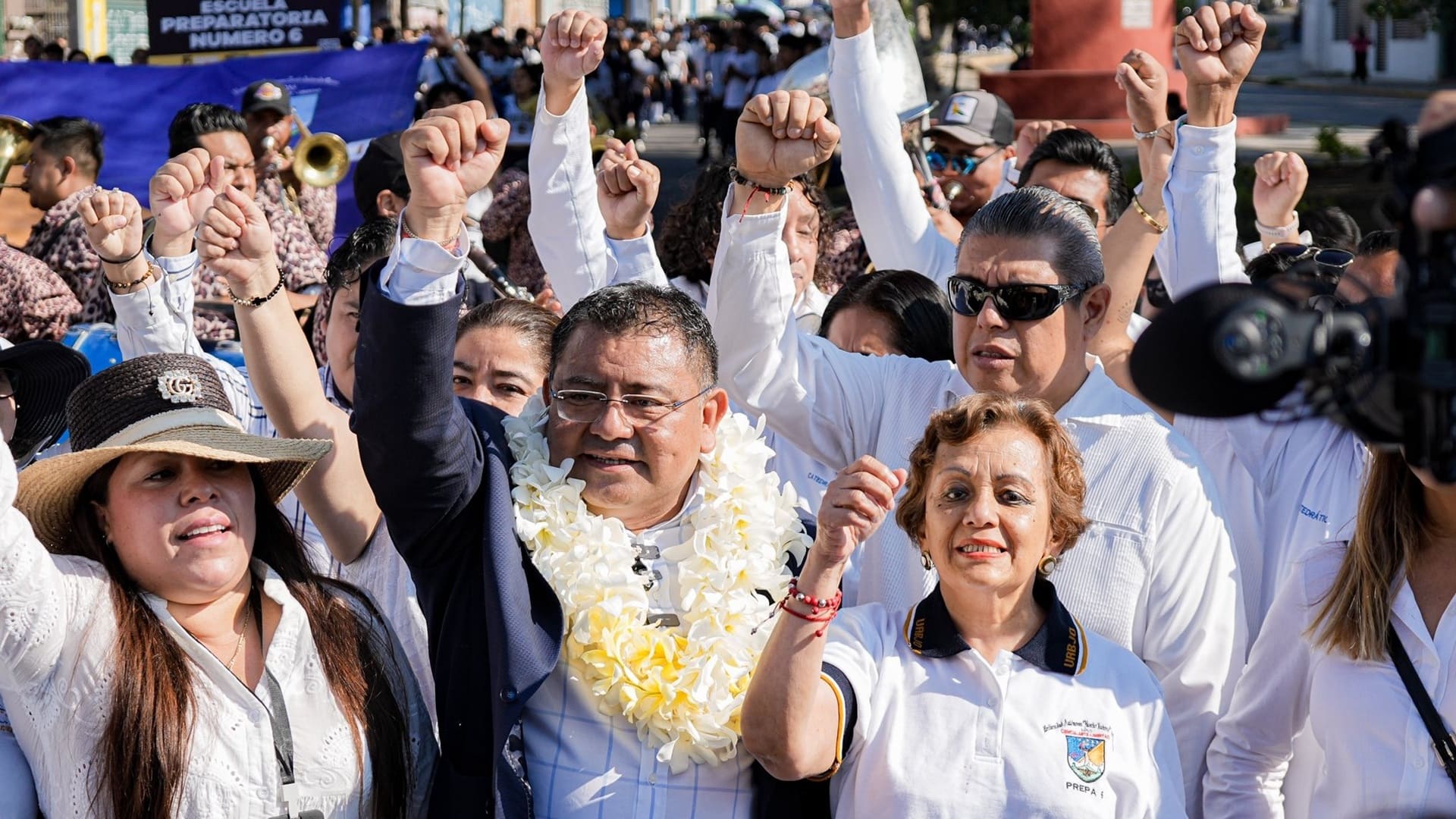 Farid Acevedo López, con una corona de flores, levanta el puño derecho acompañado de varias mujeres y hombres.