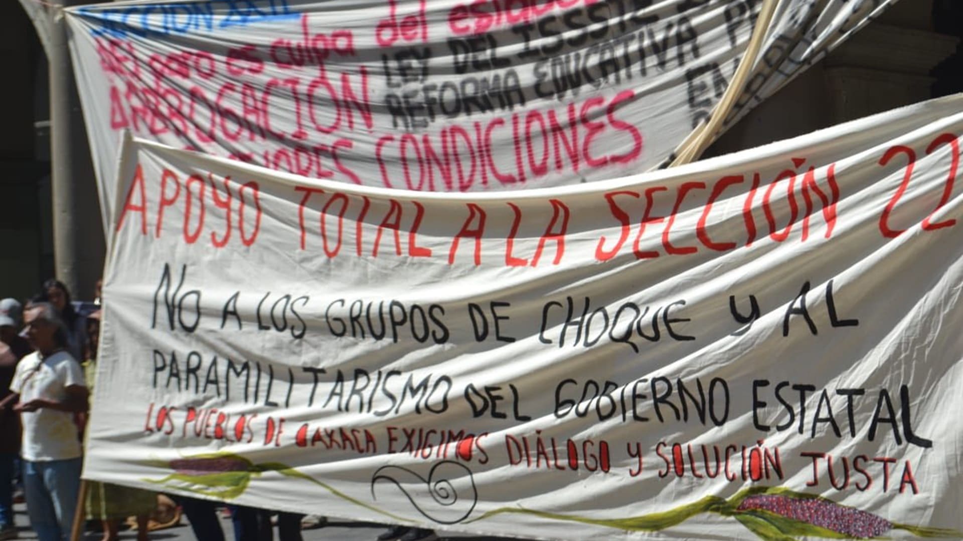 Mantas de integrantes de la CNTE en una protesta, con leyendas diversas.