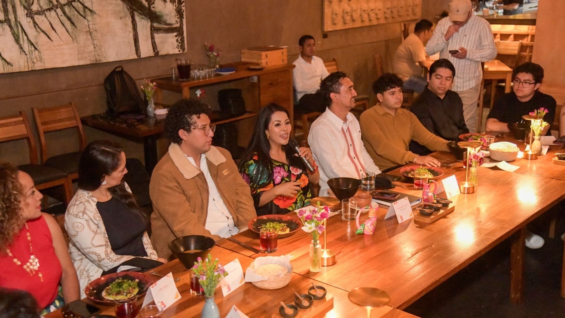 Saymi Pineda al centro de una mesa larga, donde hay más personas sentadas.