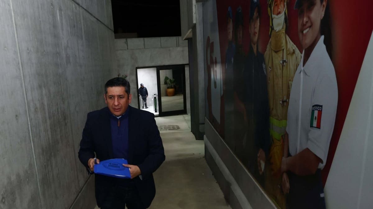 Fiscal Bernardo Rodríguez Alamilla caminando por un pasillo oscuro sosteniendo una bolsa azul en las manos