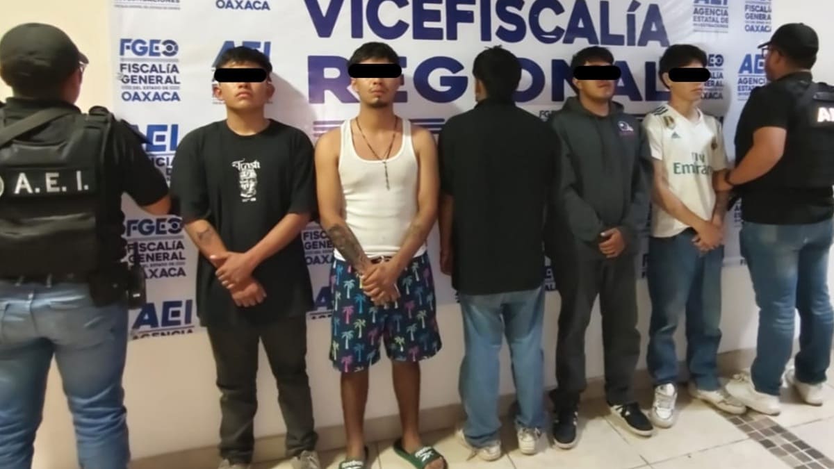 Cinco hombres jóvenes vestidos de forma casual con los ojos cubiertos por ley entre dos agentes posando para la foto