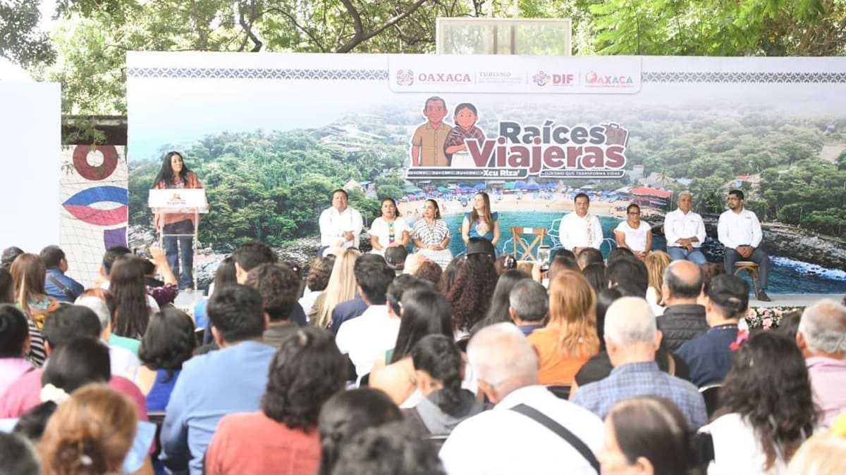 Saymi Pineda en un atril hablando a un auditorio numeroso junto a un espectacular que dice Raíces Viajeras