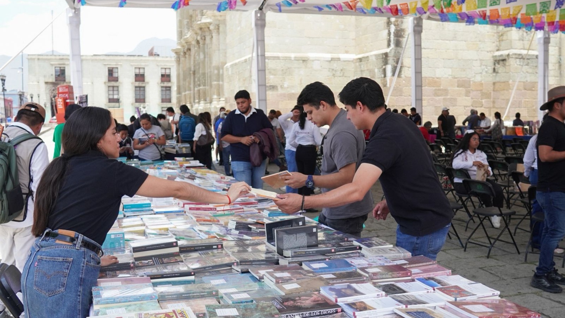 Un mercado de libros al aire libre con varias personas viendo y comprando títulos.