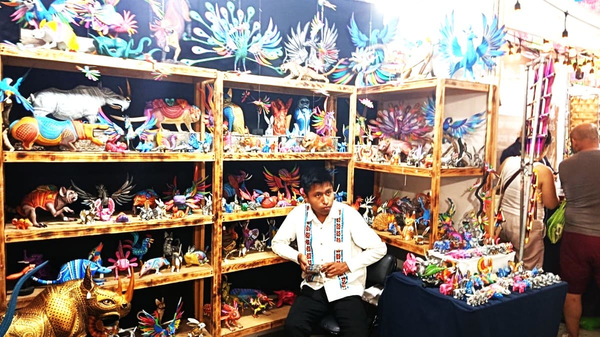 Un joven con guayabera sentado en un negocio de coloridos alebrijes