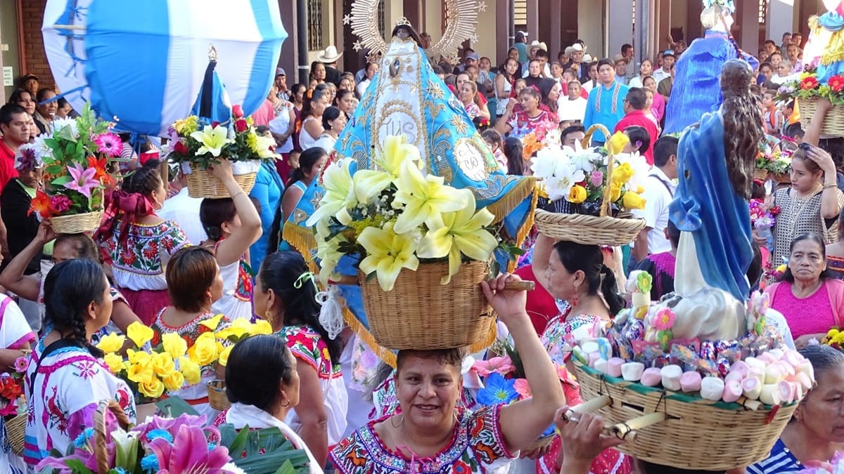 Decenas de mujeres vestidas con trajes regionales cargan canastas con flores al paso de la imagen de la Vírgen de Juquila