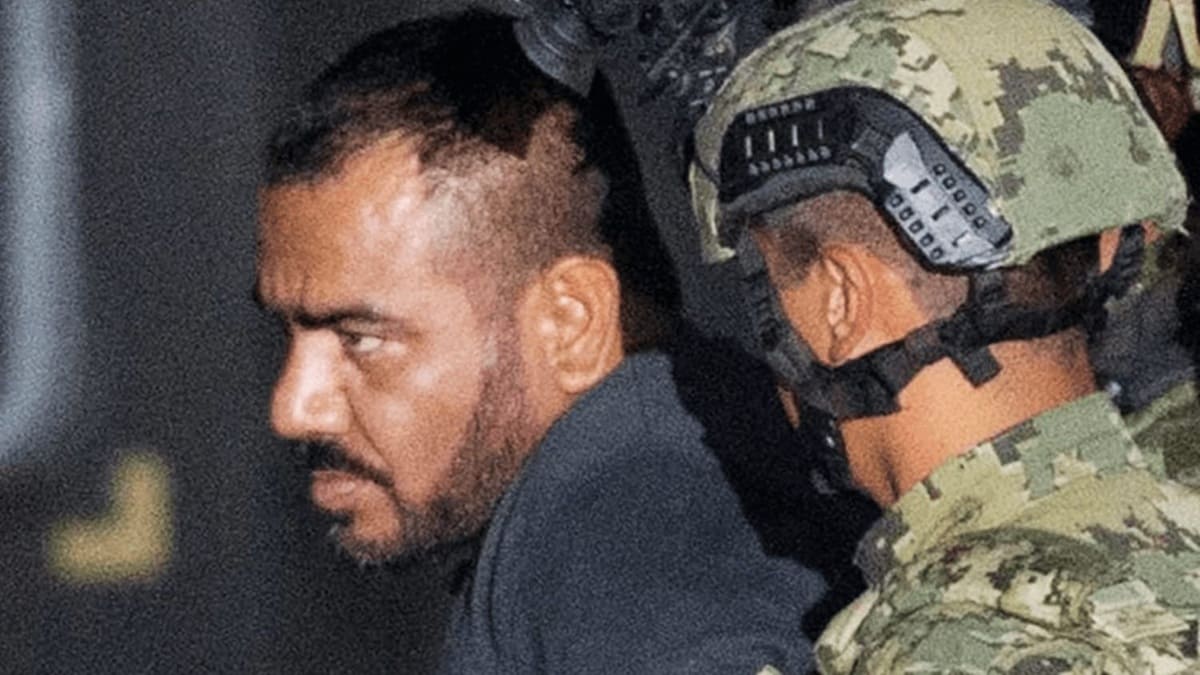 Perfil de hombre maduro con barba custodiado por un marino con uniforme y casco