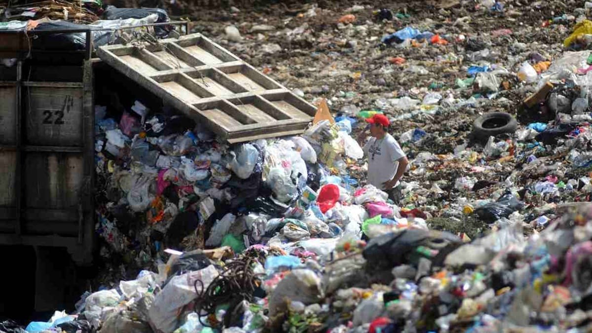 Un hombre con gorra roja y playera blanca rodeado de gran cantidad de basura y frente a un camión