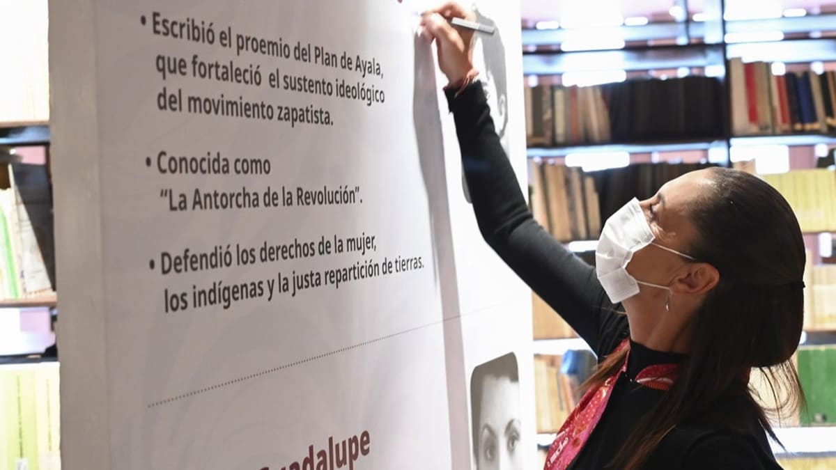 Claudia Sheinbaum con tapabocas escribe en un muro