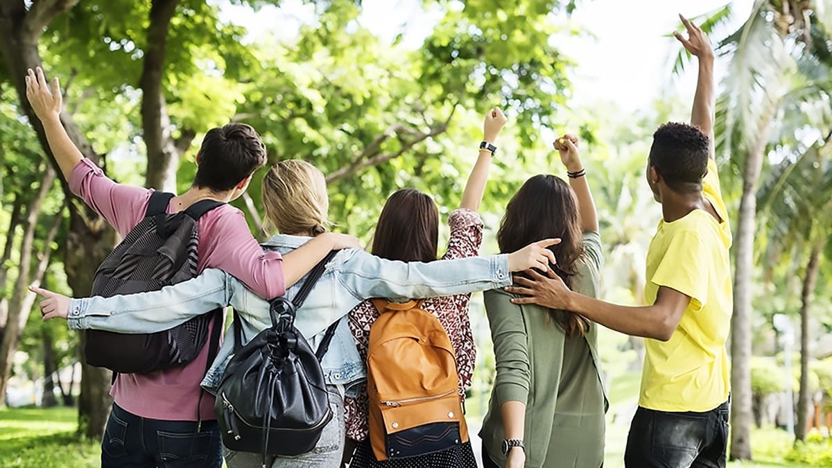 Varios jóvenes, entre hombres y mujeres, saluda con las manos en alto en un parque