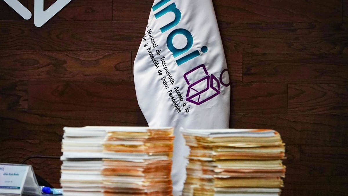 Papeles apilados sobre una mesa junto a la bandera con las letras INAI