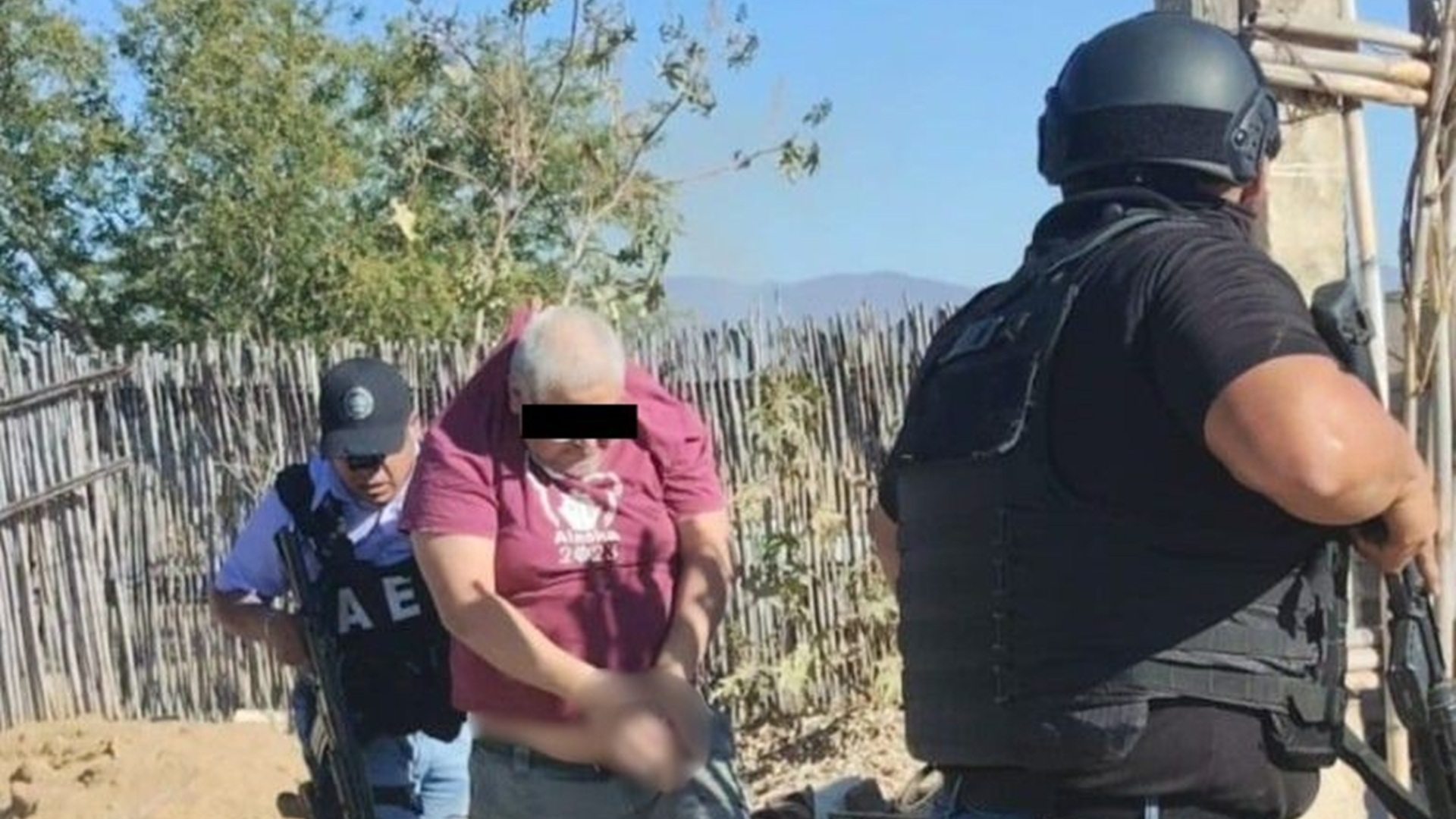 Hombre con playera guinda y el rostro protegido, es detenido y conducido por dos policías de Oaxaca.