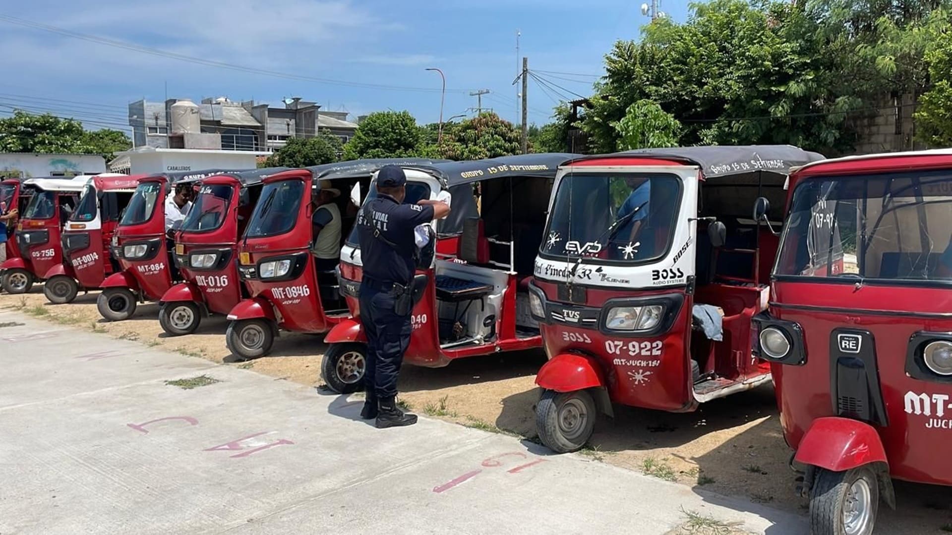 Policía con uniforme parado frente a una decena de mototaxis de color rojo en una calle.