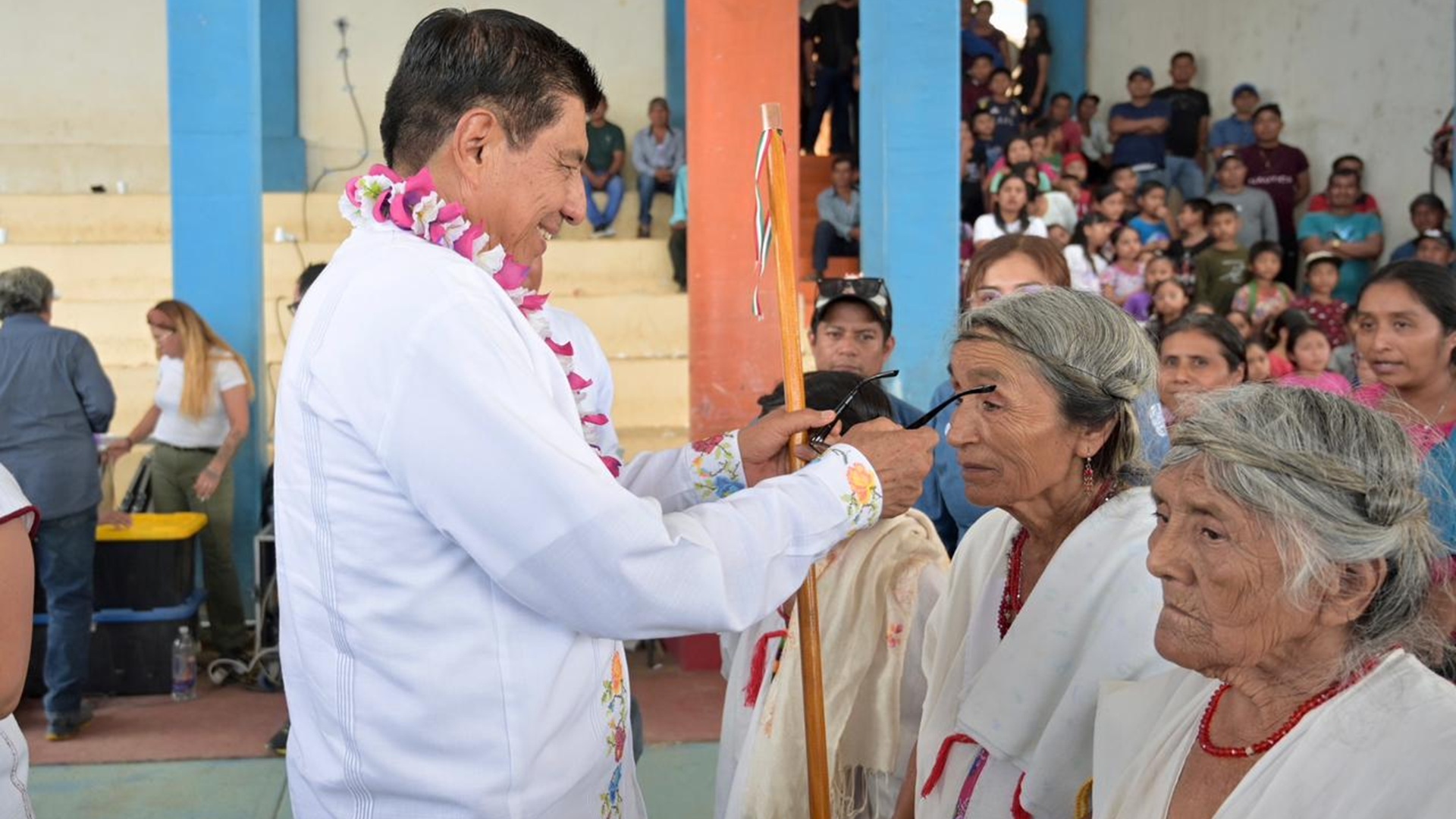 Salomón Jara vestido de blanco pone unos lentes a una mujer adulta mayor, junto a otras mujeres de similares características.