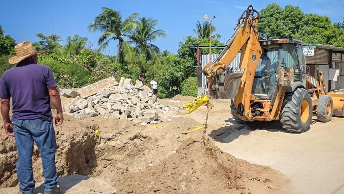 Un hombre con sombrero y pantalón de mezclilla observa una máquina de construcción realizando trabajos en una calle