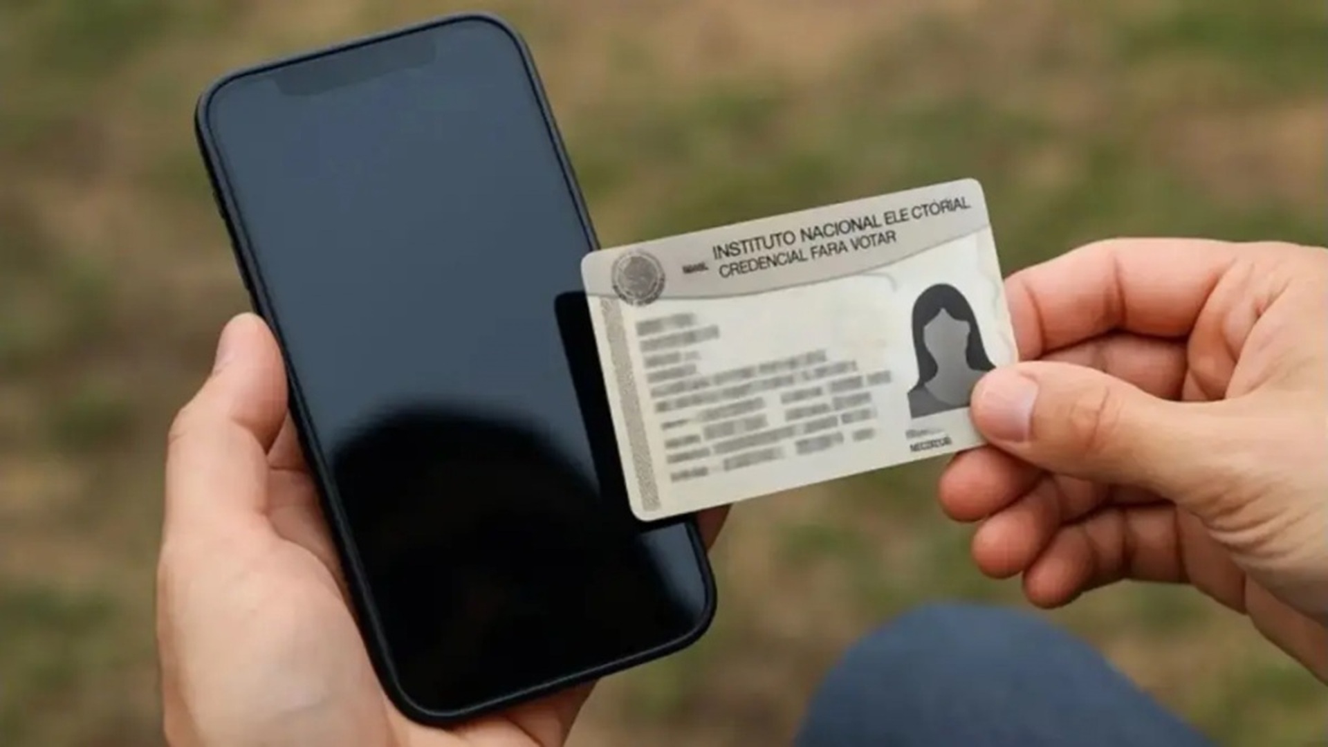 Una mano sosteniendo un celular aparado y otra mano sosteniendo una réplica de una credencial del INE.