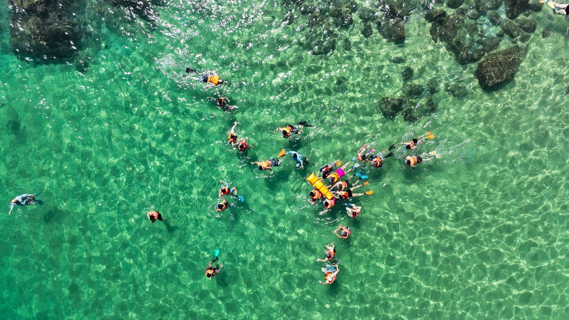 Perspectiva aérea de nadadores en el océano, con olas suaves y un cielo despejado.